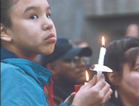 Photo of young girl holding a lighted candle. She is part of a larger group of people at an event commemorating victims of crime.