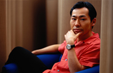 Photo of an Asian man sitting on a couch, resting his chin on his hand.