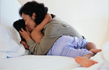 Asian American mother comforting her child in bed.
