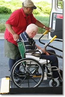 Man helping another man in a wheelchair get into a car